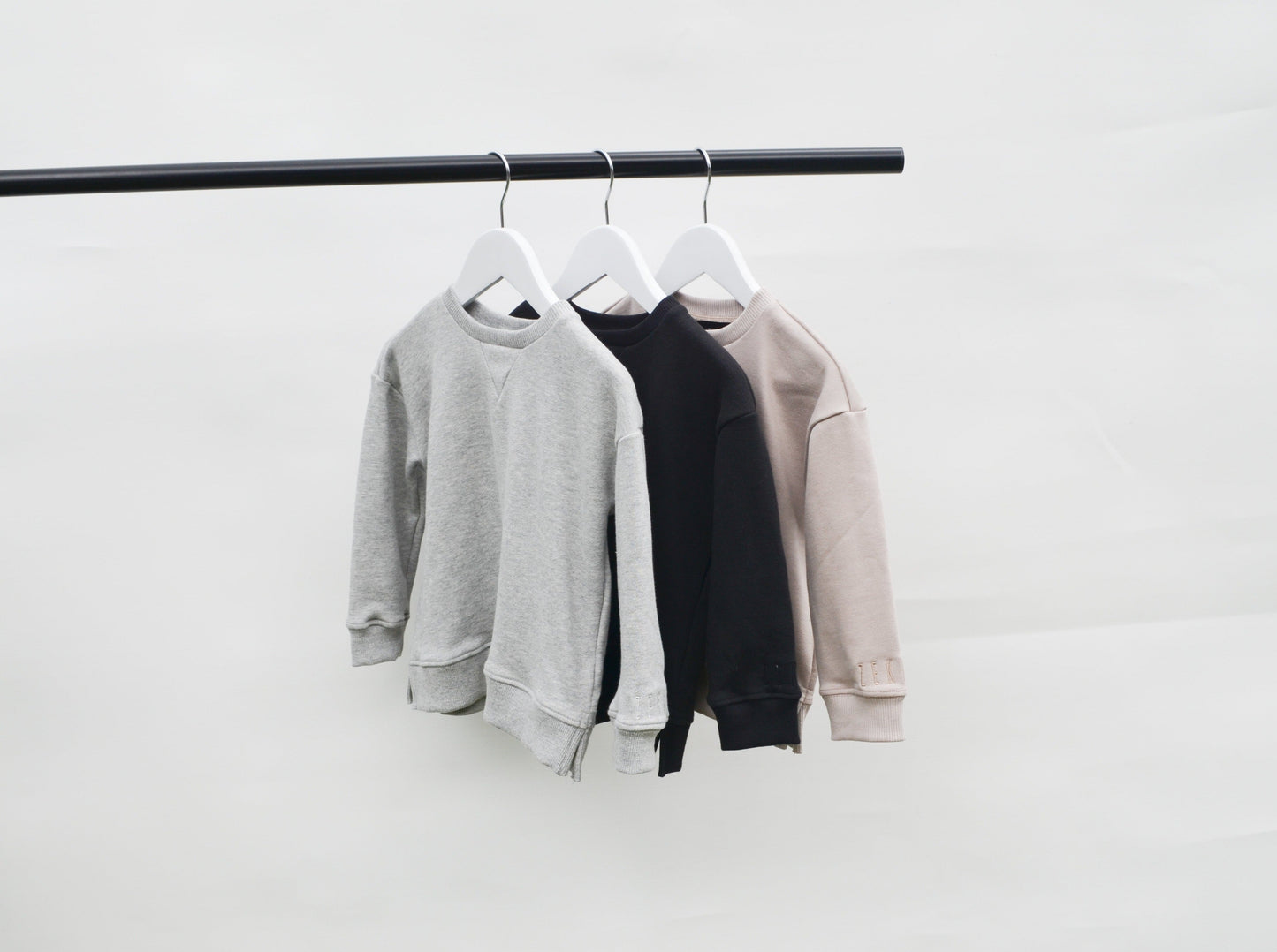 Grey, black and smokey colour longline jumpers on coat hangers hanging from pole