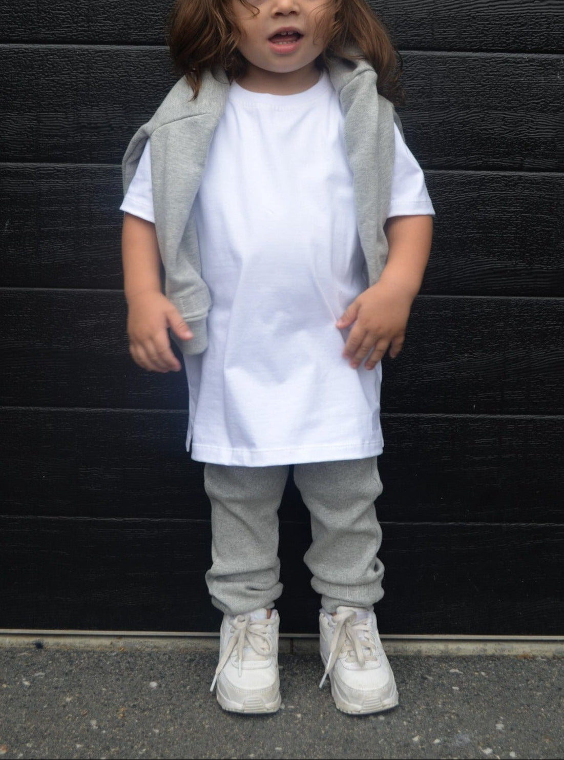 Boy wearing white longline t-shirt with grey jumper on shoulders and grey loose leggings