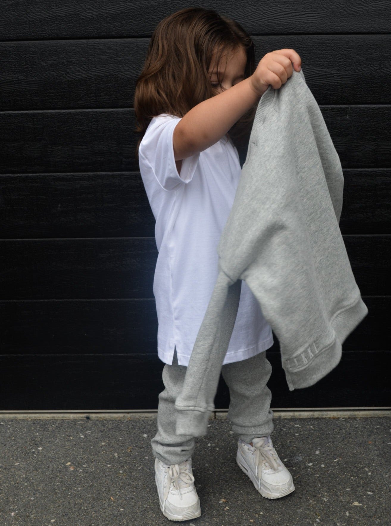 Boy carrying grey longline jumper, wearing white longline t-shirt and grey loose legging