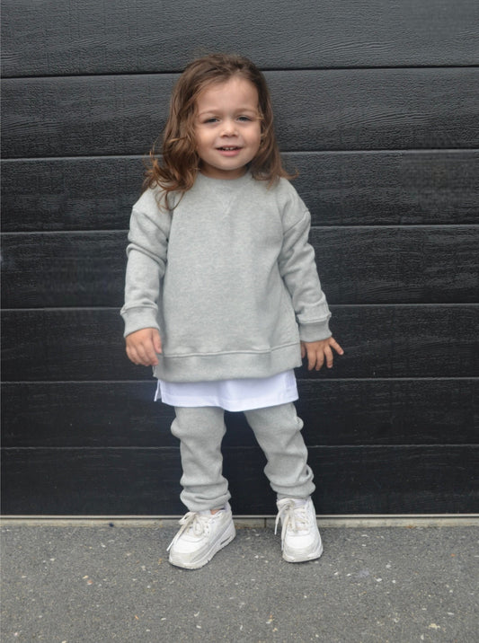 Boy wearing grey longline jumper, wearing white longline t-shirt and grey loose legging/casual pants